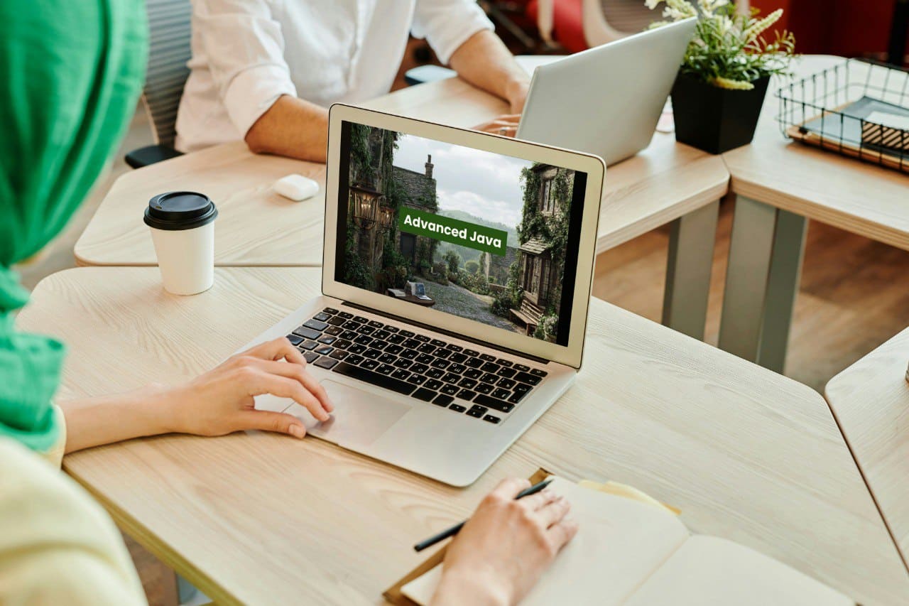 Person using a laptop with 'Advanced Java' on screen in a casual office setting