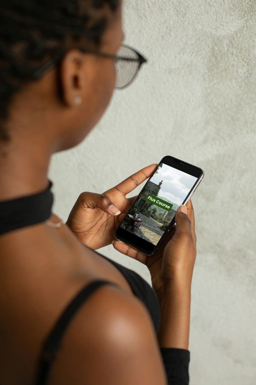 Person holding a smartphone  displayed 'Flux Course' on the screen against a neutral background