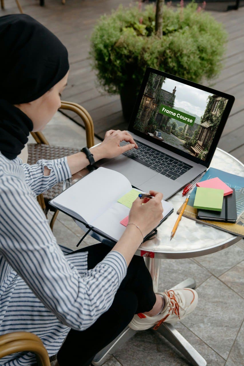 Person sitting at a table outdoors using a laptop with a course displayed on the screen.